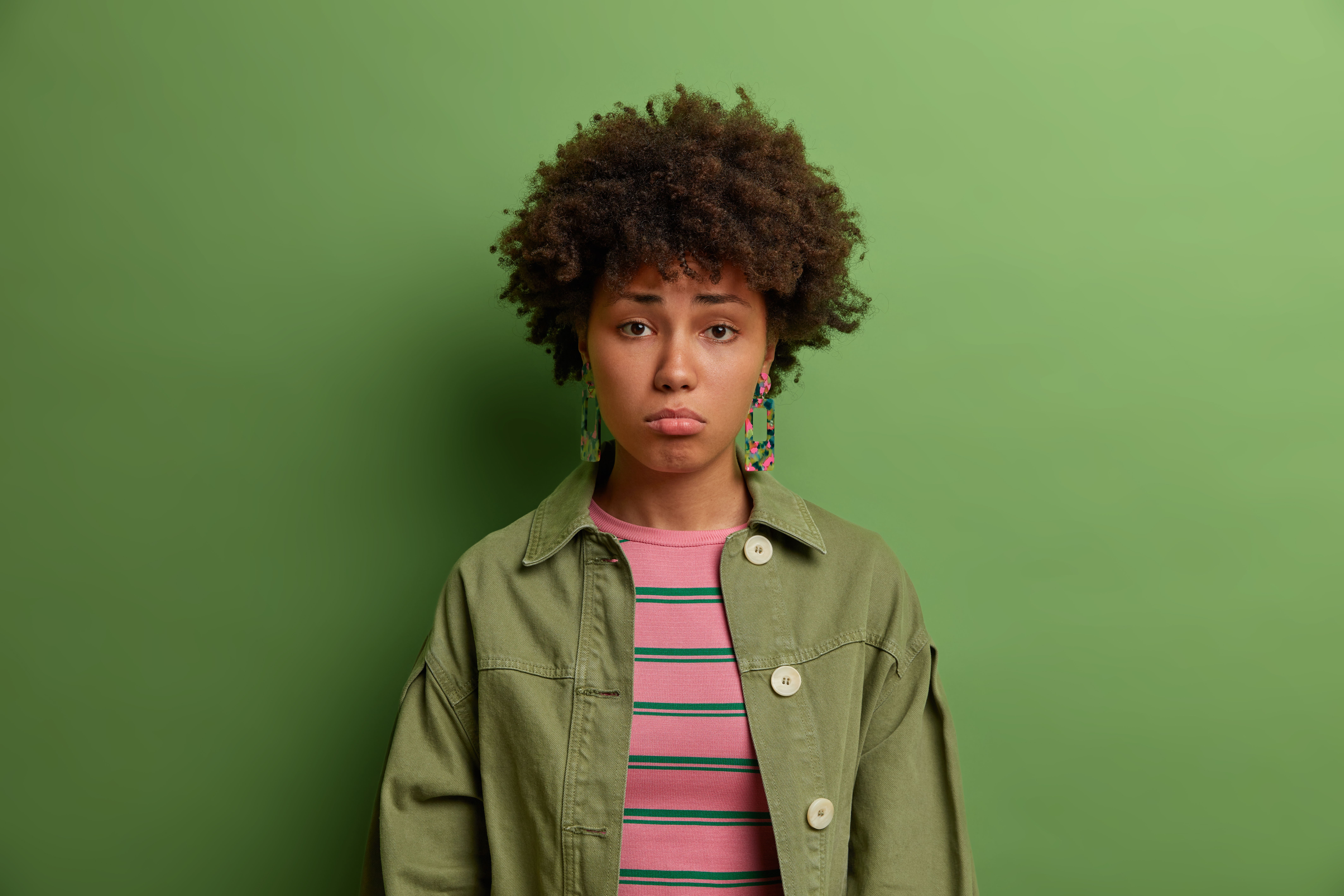 Junge Dame mit Afro steht traurig vor grüner Wand